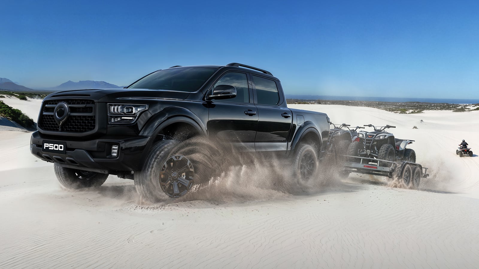 A black GWM P500 double cab powering through white coastal dunes, towing a trailer with two quad bikes