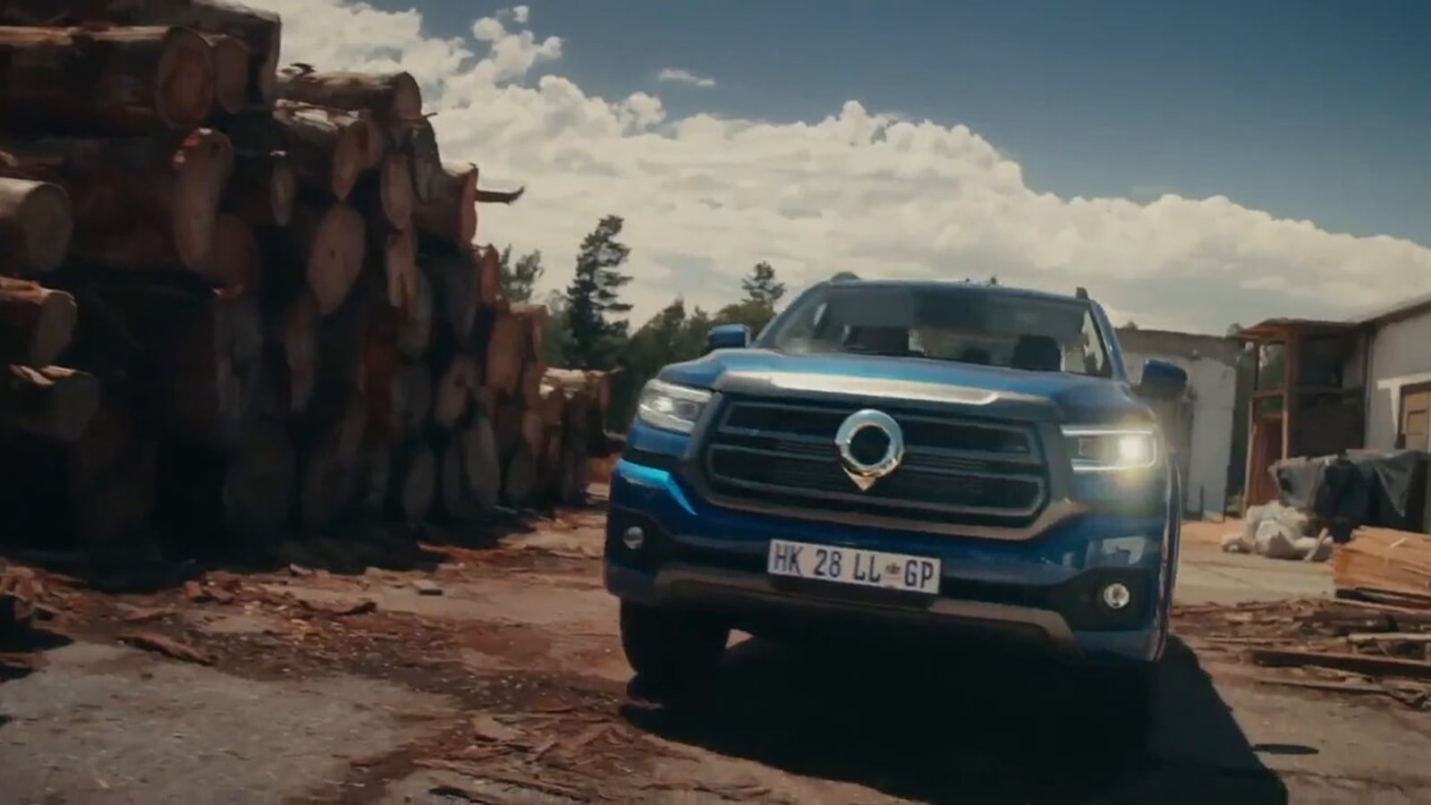 A blue GWM P300 double cab parked at a timber yard with stacked pine logs behind it