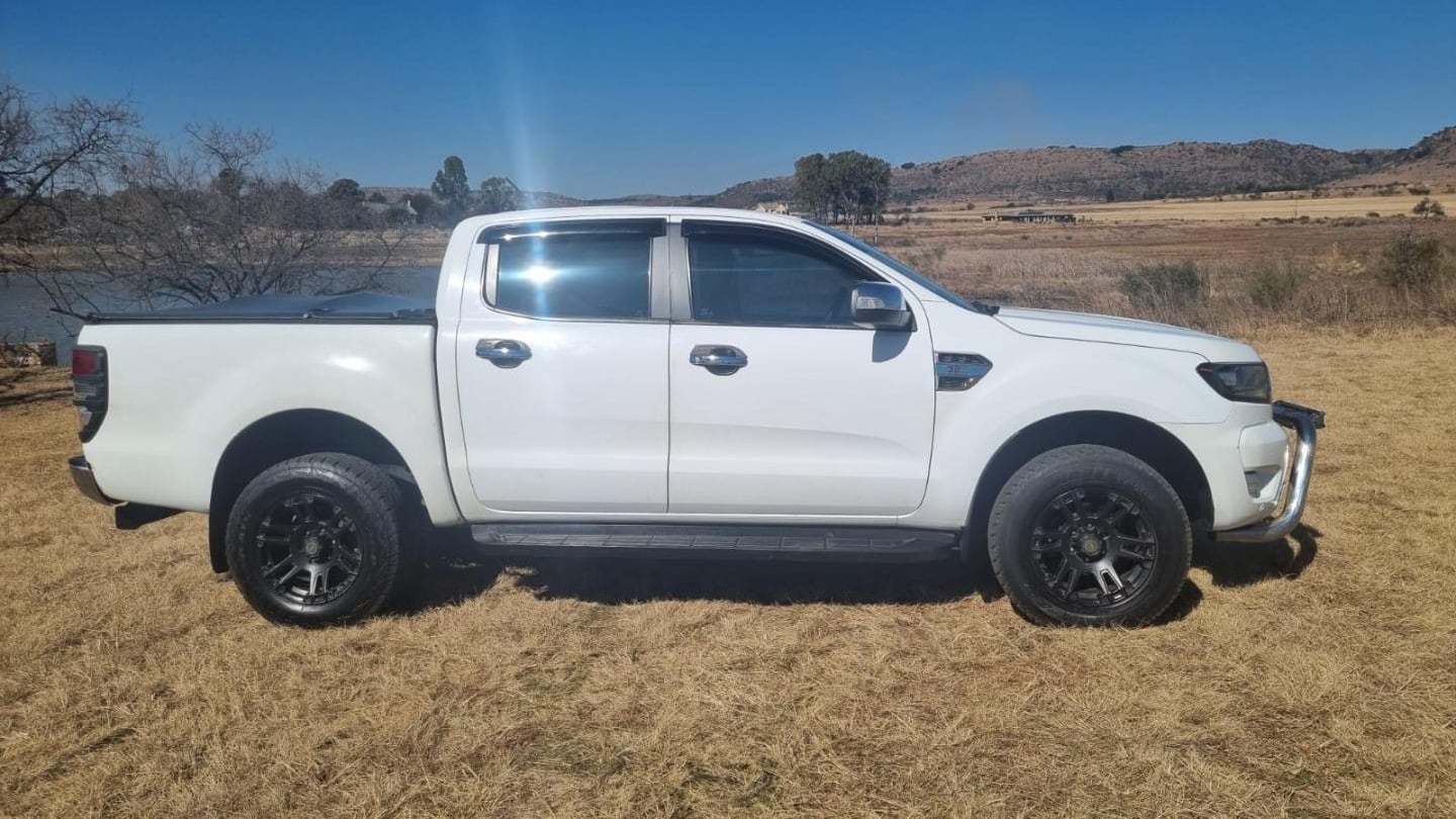 A white 2019 Ford Ranger 3.2 XLT double cab parked side-on on dry winter veld beside a farm dam under a blue highveld sky