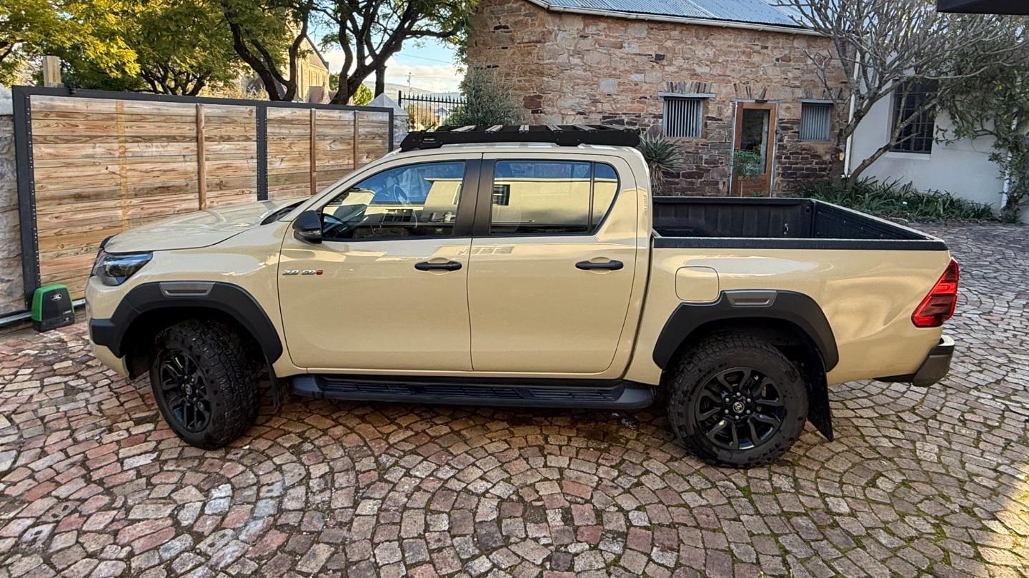A beige 2023 Toyota Hilux 2.8 GD-6 Legend RS double cab parked side-on on cobbles in front of a sandstone farmhouse