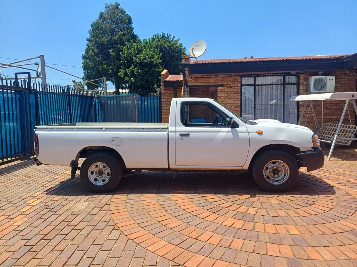 Side view of a white 2019 Nissan NP300 2.5 TDi long-bed single cab on steel wheels, parked in a suburban driveway in Gauteng