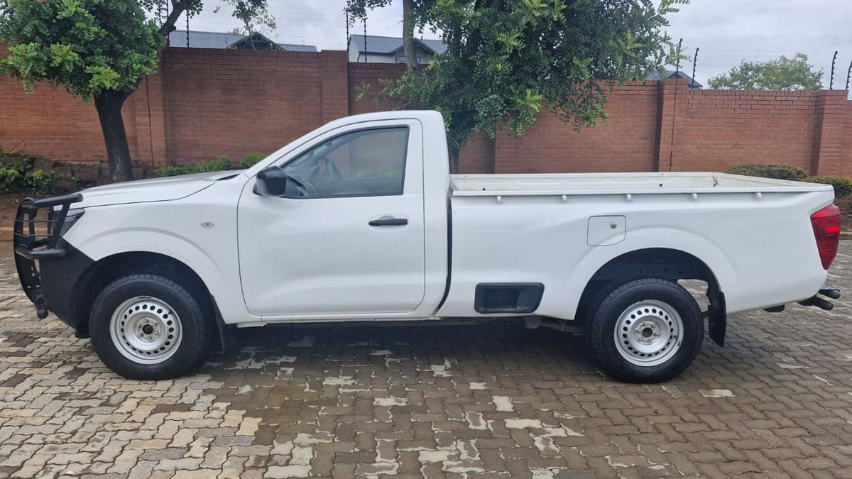 Side view of a white Nissan Navara single cab with a black bull bar and steel wheels, parked on brick paving against a face-brick wall in Pretoria