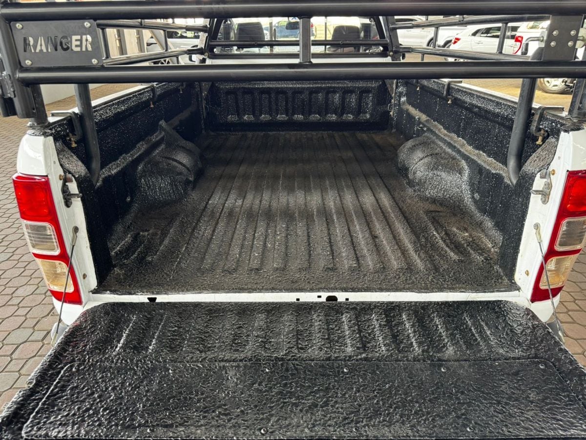 Looking down into the rubberised load bin of a white Ford Ranger single cab, with black cattle rails and RANGER cut into the headboard