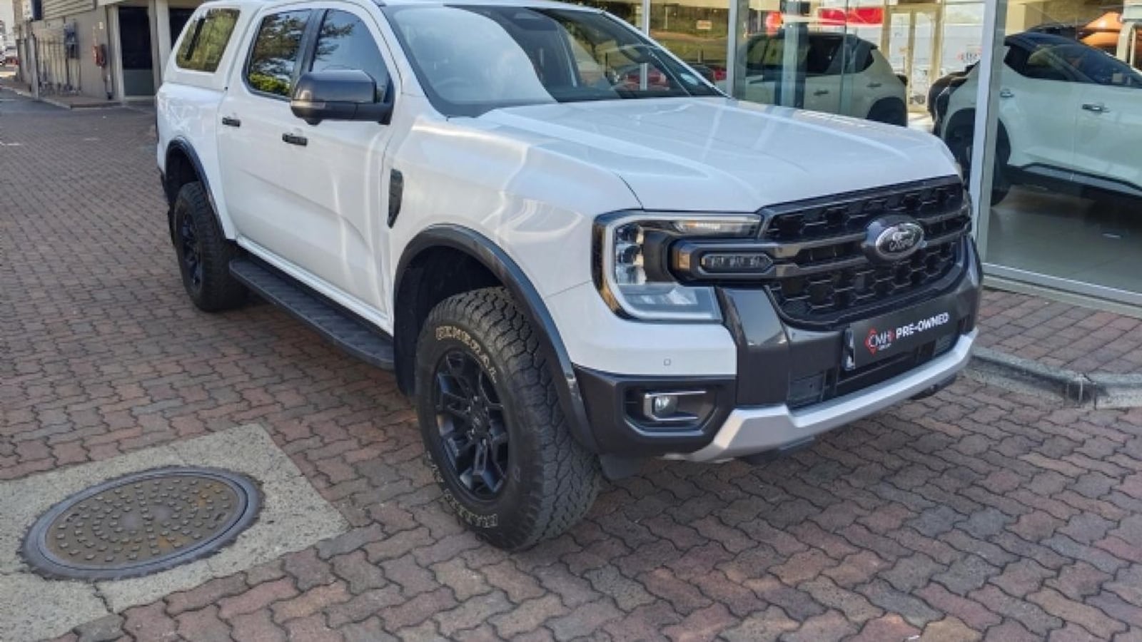 A white 2024 Ford Ranger 2.0 Bi-Turbo Tremor 4x4 double cab with a canopy, black grille and General Grabber all-terrain tyres, parked on paving outside a dealership in Pietermaritzburg