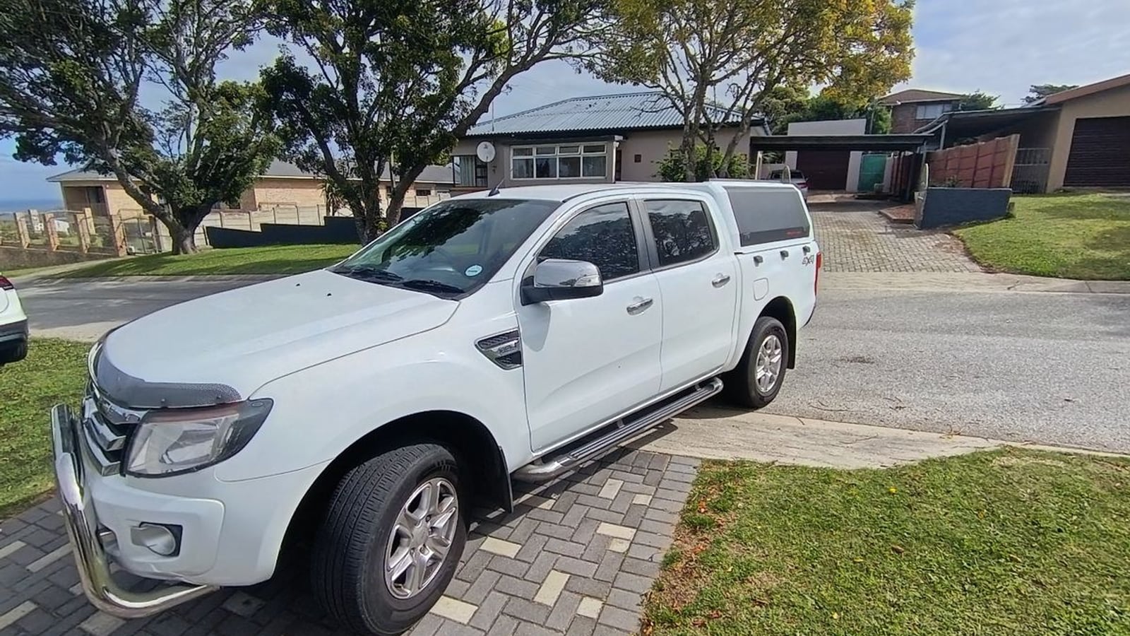 A white 2013 Ford Ranger 3.2 TDCi XLT 4x4 automatic double cab with a canopy, nudge bar and bonnet guard, parked in a suburban driveway in Gqeberha