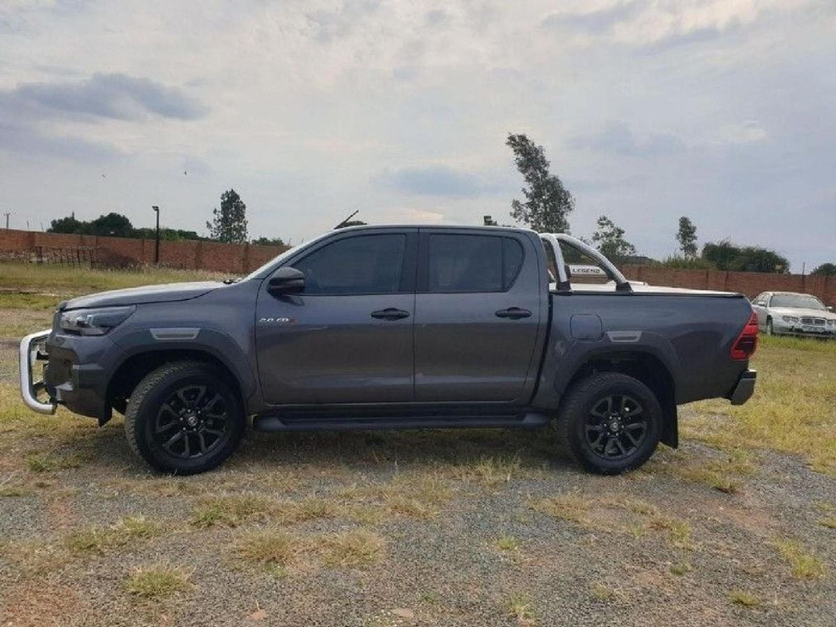 A grey 2022 Toyota Hilux 2.8 GD-6 Legend automatic double cab with a chrome nudge bar and sports bar, side on, on winter grass in a walled yard in De Deur