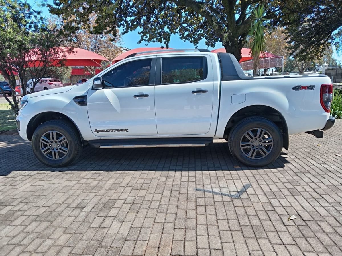 A white 2022 Ford Ranger 2.0 Bi-Turbo Wildtrak 4x4 automatic double cab, side on, on brick paving under a jacaranda in Johannesburg