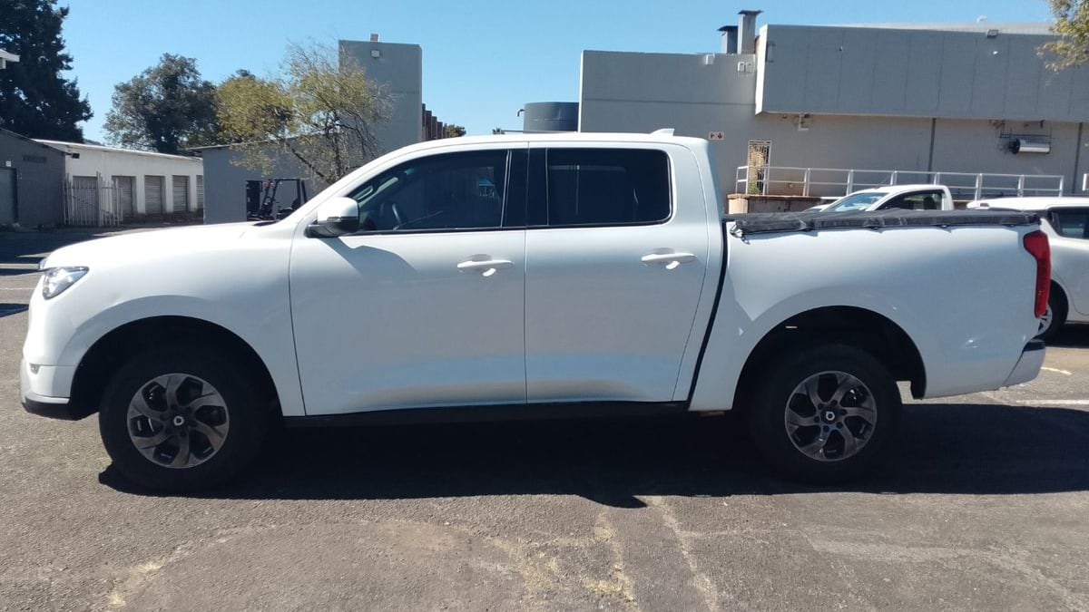 A white 2023 GWM P-Series CV 2.0 TD SX double cab, side on, parked on tar at an industrial park in Johannesburg with a warehouse behind it