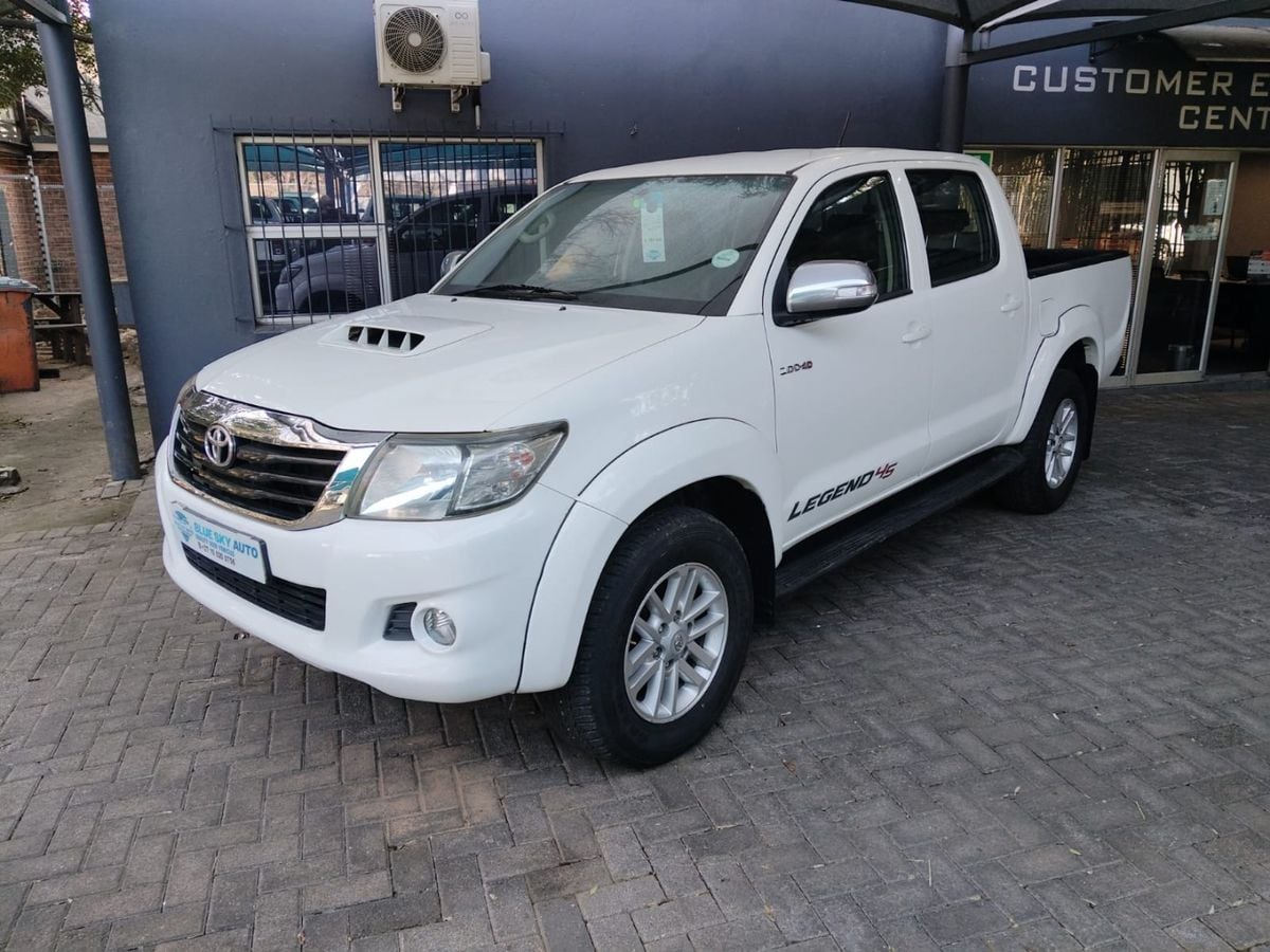 A white 2015 Toyota Hilux 3.0 D-4D Legend 45 4x4 manual double cab with the bonnet scoop, parked under a shade net at a small Johannesburg dealer