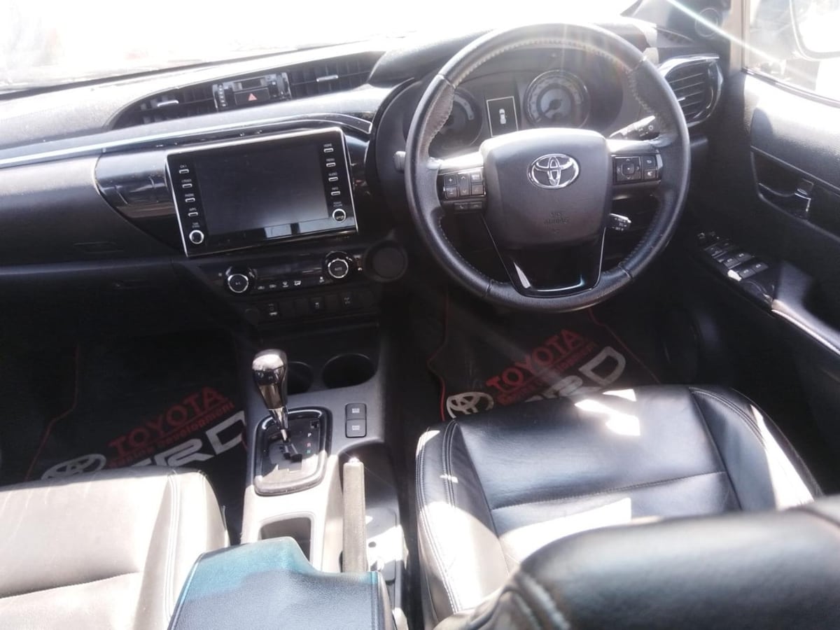 The dashboard and centre console of a 2020 Toyota Hilux Legend 50 seen from the open passenger door, with the eight-inch touchscreen, piano-black centre stack, leather seats and the six-speed automatic lever