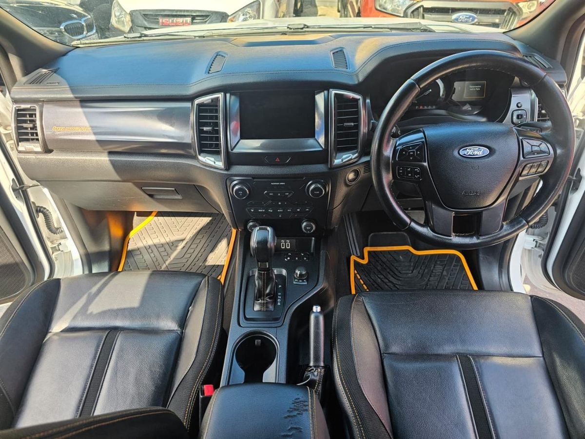 The dashboard and centre console of a 2020 Ford Ranger Wildtrak seen from the open passenger door, with the SYNC 3 touchscreen, leather seats with orange stitching and the ten-speed automatic lever