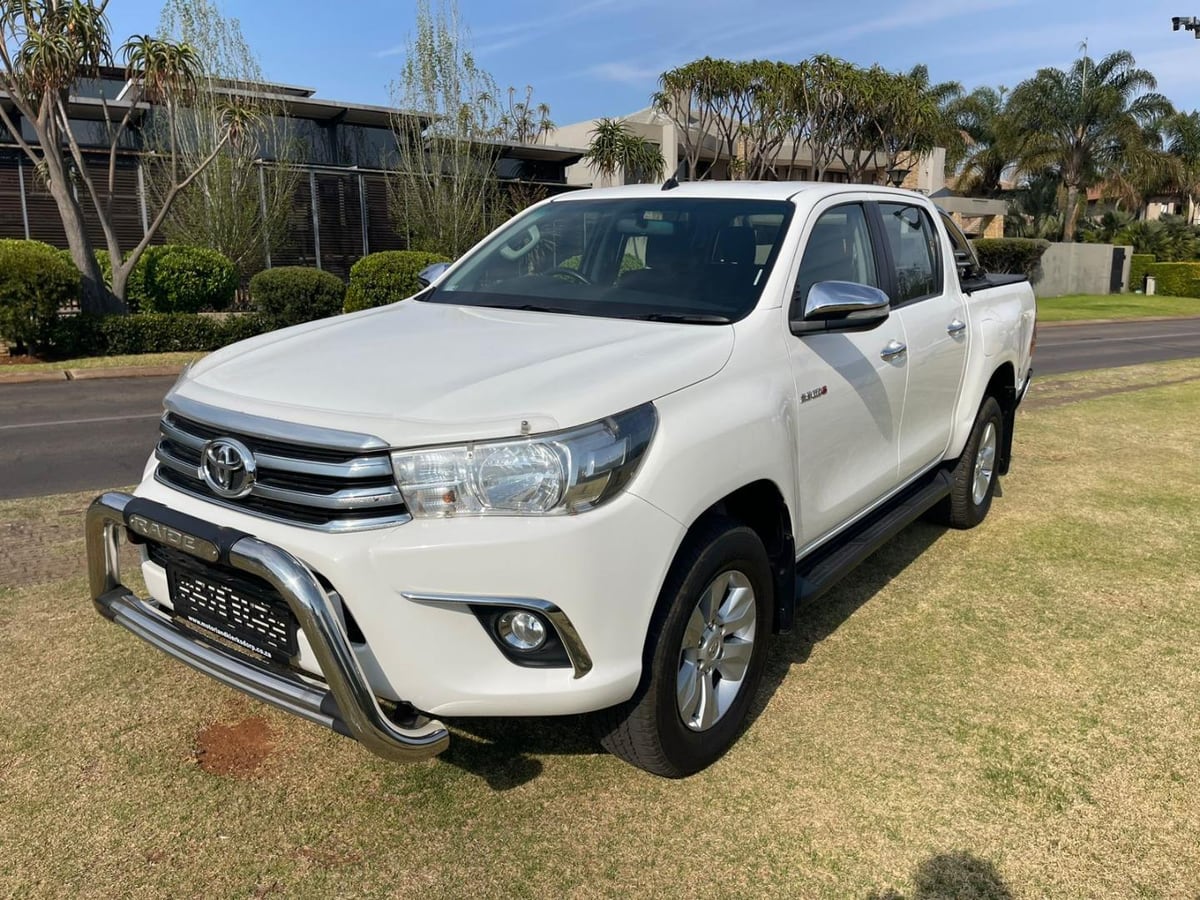 A white 2016 Toyota Hilux 2.8 GD-6 Raider automatic double cab with a chrome nudge bar, parked on an estate verge in Gauteng