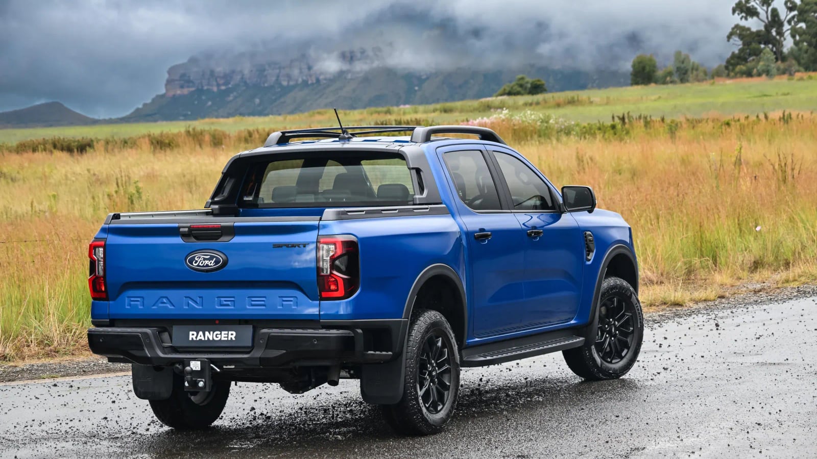 Rear view of a Ford Ranger double cab on a gravel road with mountains behind it